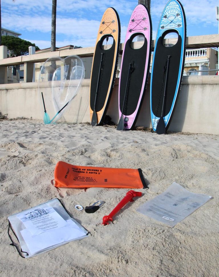 Paddle board gonflable avec fenêtre transparente en exposition sur le sable devant le kit safeboxforbeach étaler sur le sable